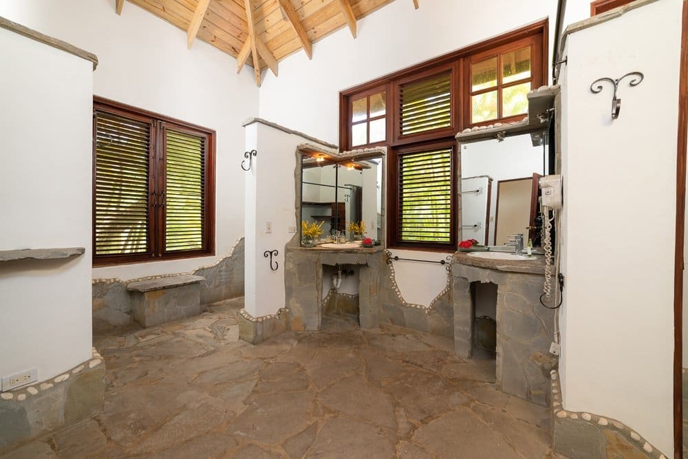 buyDRproperty Spacious bathroom with stone floors, wooden shutters, and two sinks. Sosua Real Estate