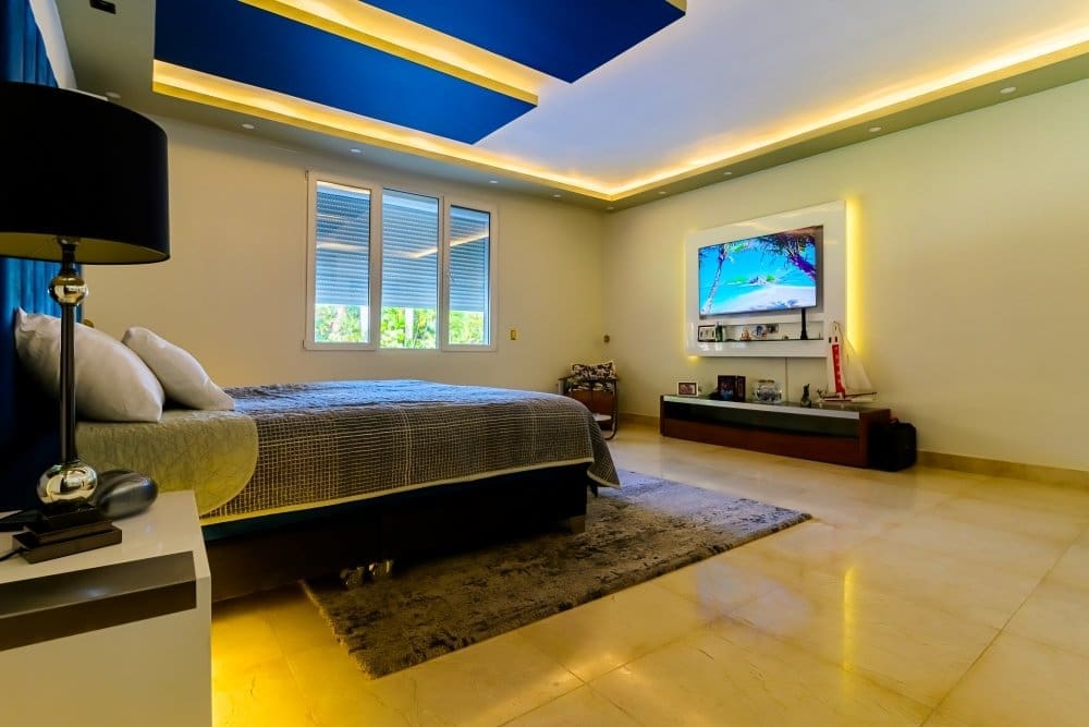 buyDRproperty Modern bedroom with king-size bed, large TV, and blue ceiling accents. Sosua Real Estate