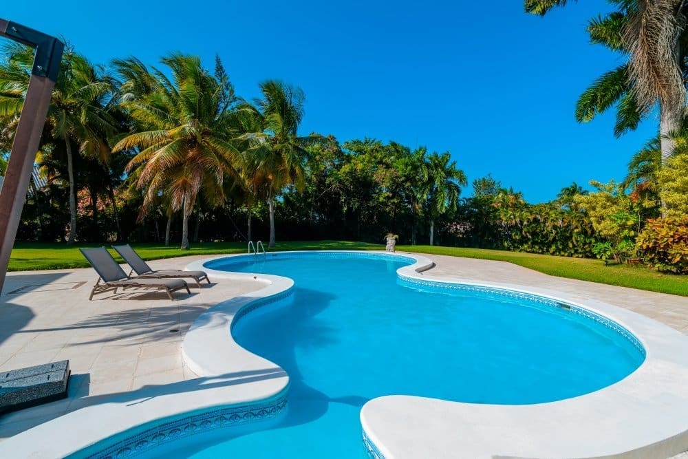 buyDRproperty Luxury swimming pool with lounge chairs and palm trees under a clear blue sky. Sosua Real Estate