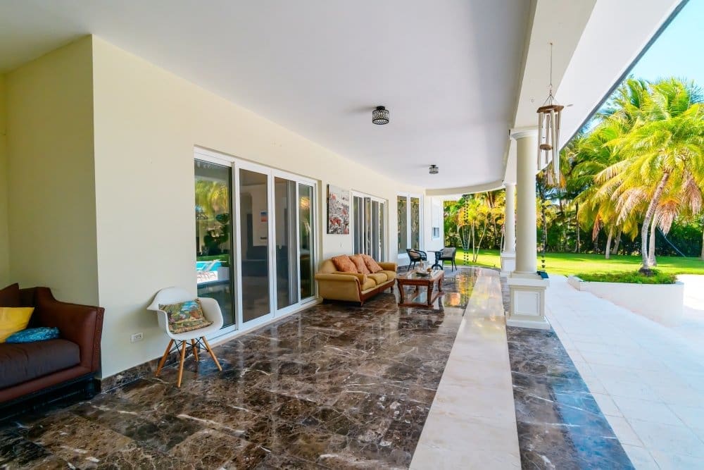 buyDRproperty Spacious covered patio with marble flooring, comfortable seating, and tropical palm trees. Sosua Real Estate
