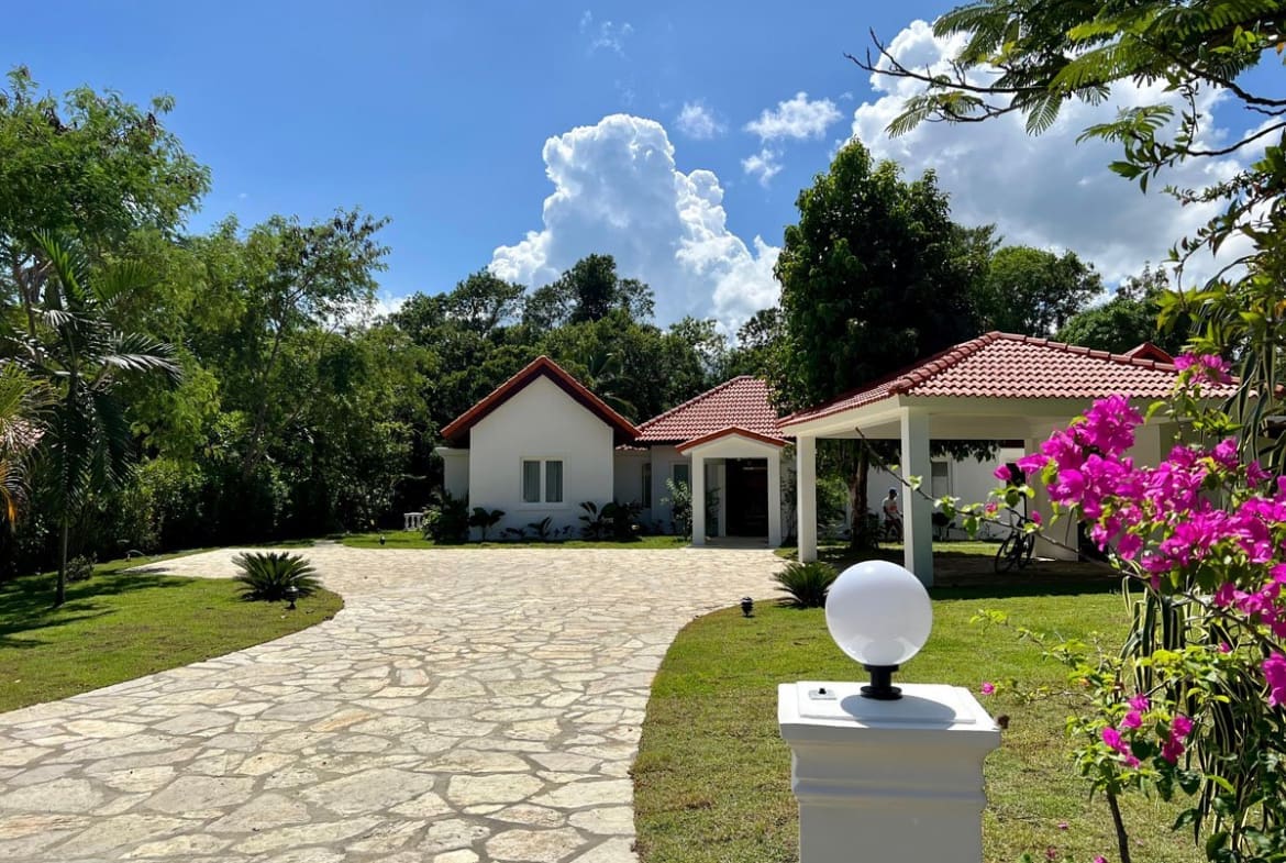 buyDRproperty White modern house with red tile roof, stone driveway, and vibrant pink bougainvillea. Sosua Real Estate