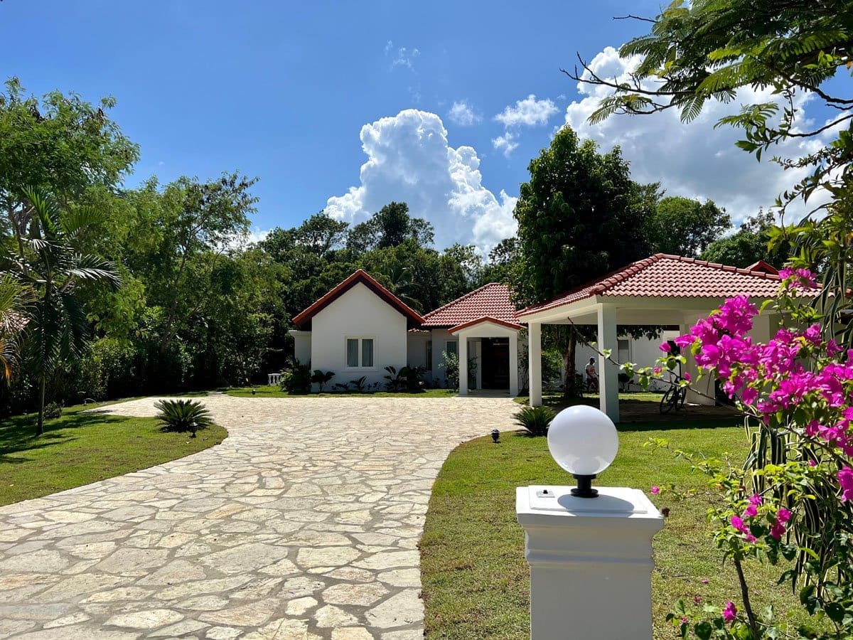 buyDRproperty White modern house with red tile roof, stone driveway, and vibrant pink bougainvillea. Sosua Real Estate