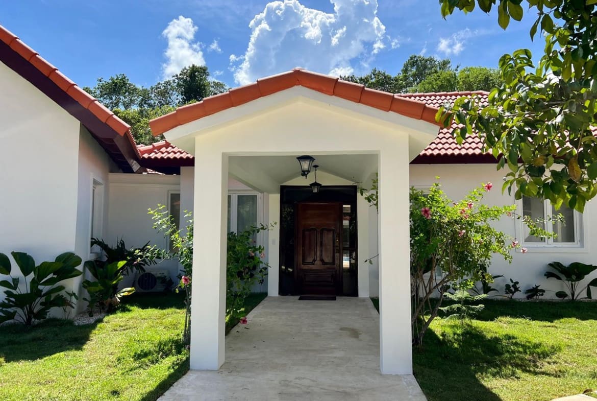 buyDRproperty Tropical villa entrance with lush greenery and tiled roof Sosua Real Estate