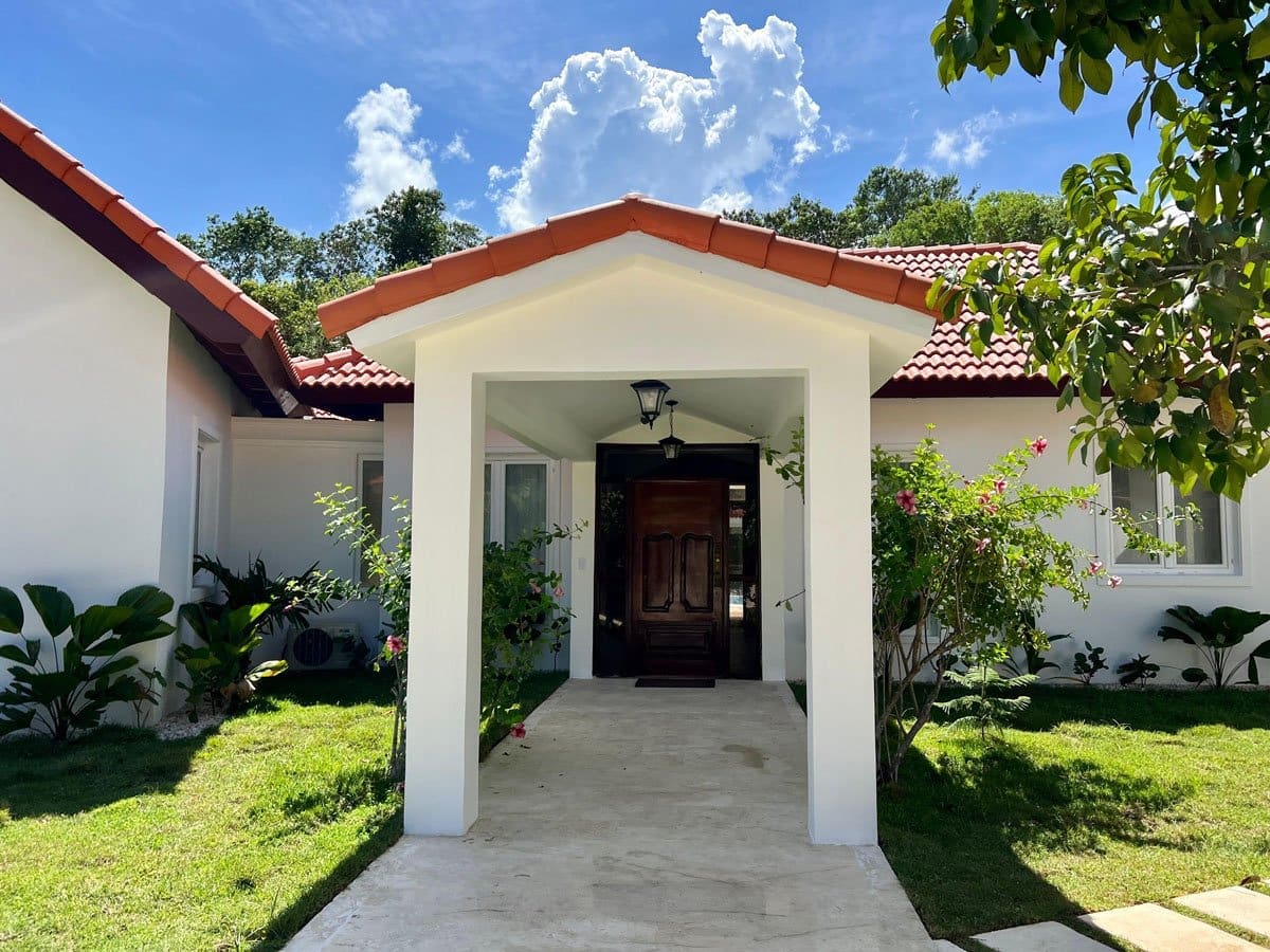 buyDRproperty Tropical villa entrance with lush greenery and tiled roof Sosua Real Estate