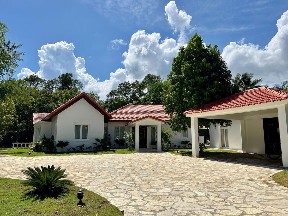 buyDRproperty White modern house with red tile roof and stone driveway in lush green landscape. Sosua Real Estate