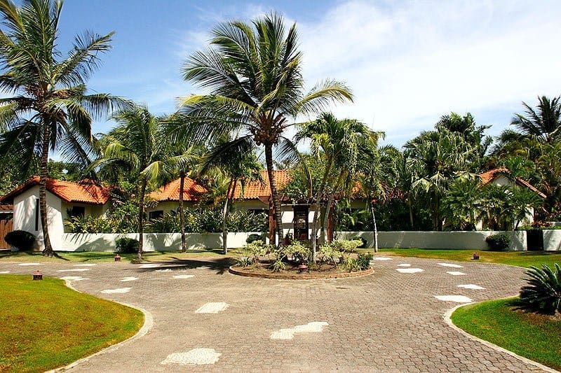 buyDRproperty Tropical resort entrance with palm trees, white walls, and tiled driveway. Sosua Real Estate