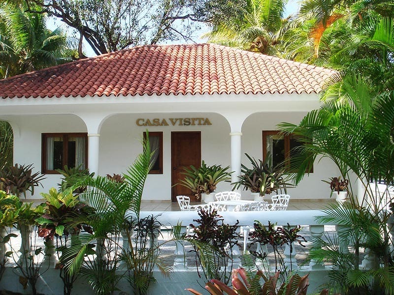 buyDRproperty Casa Visita: white tropical villa with red tile roof and lush greenery. Sosua Real Estate